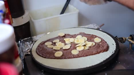 Hands-close-up-cutting-banana-slices-falling-into-delicious-Nutella-crepe