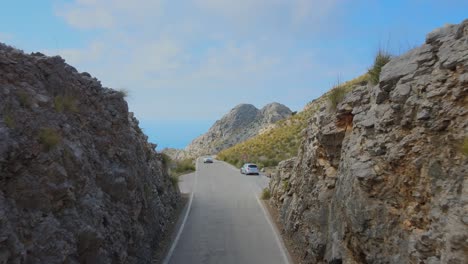 Drone-flying-in-between-two-rock-formations-on-top-of-a-mountain-road-following-a-car-at-Sa-Calobra,-Mallorca,-Spain