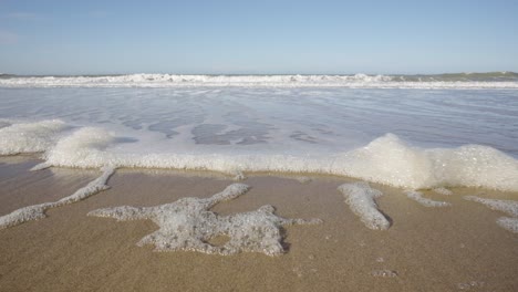 POV-of-gentle-foamy-waves-moving-up-towards-a-pristine-beach-on-the-North-Sea,-Belgian-coast