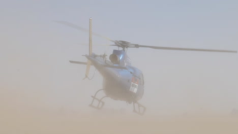 Extremely-dusty-location-with-blue-helicopter-take-off-and-car-drives-by
