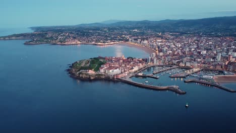 Gijon-aerial-zoom-out-view-at-the-Galicia-capital-during-night,-city-center-and-harbor-illuminated