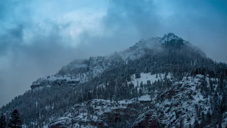 Time-Lapse-of-Cold-WInter-Landscape-in-Mountains,-Dark-Clouds-Moving-Above-Snow-Capped-Hills-and-Forest