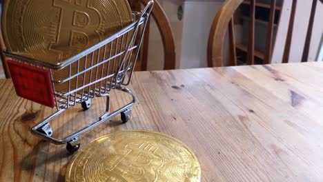 Golden-bitcoin-crypto-currency-coins-in-tiny-shopping-trolley-on-kitchen-table-concept-looking-down-orbit-left