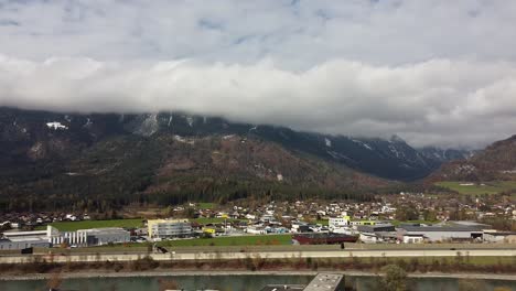 Drone-Pan-De-Izquierda-A-Derecha-Sobre-Brixlegg-En-Tirol,-Montañas-Con-Nubes-Y-La-Posada-Del-Río