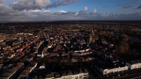 Aerial-zoom-and-approach-over-historic-tower-town-Zutphen-with-cityscape-seen-from-above-river-IJssel-with-stark-shadow-contrast-and-dramatic-clouds-above