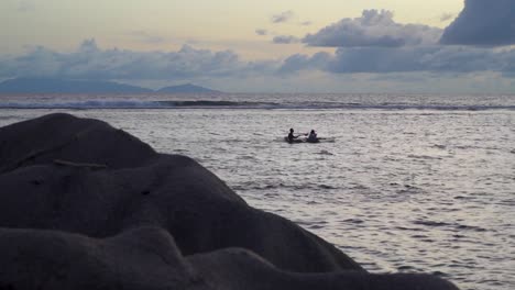 Gente-Haciendo-Kayak-Al-Atardecer-Frente-A-La-Costa-De-Una-Isla-Tropical