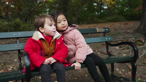 View-of-a-little-boy-and-a-little-girl-smiling,closing-up-to-pose-for-a-photo-on-a-black-color-bench-in-a-park-on-a-wintry-evening