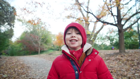 Static-view-of-a-cute-little-boy-smiling-and-posing-for-a-shot-wearing-red-jacket-on-the-pathway-by-the-side-of-the-road-on-a-wintry-afternoon