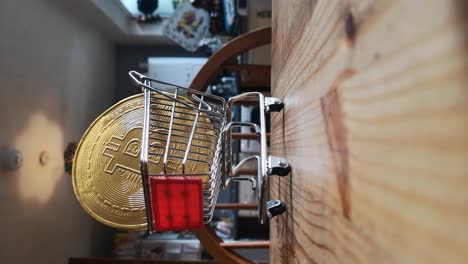 Vertical-clip:-Gold-bitcoin-crypto-currency-in-tiny-shopping-cart-on-kitchen-table-concept-slow-push-in-low-angle