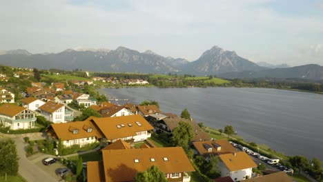 Picturesque-Aerial-View-of-European-Village-on-a-Lake-with-Mountains-in-Background