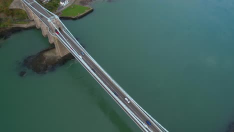Scenic-drone-shot-at-Menai-Suspension-Bridge,-cars-crossing,-cloudy-day