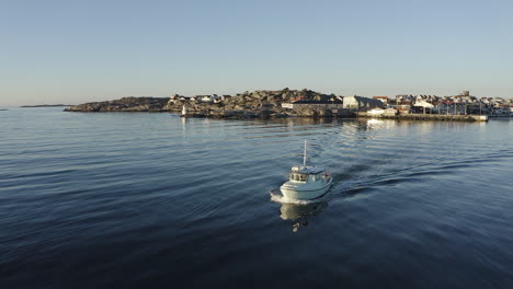 Drone-shot-of-a-small-white-motor-boat-heading-out-to-open-sea-at-Gothenburg-archipelago,-Sweden
