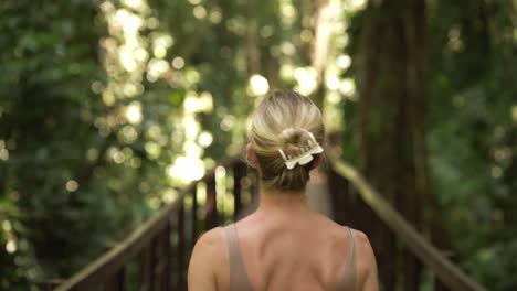 Gorgeous-blond-woman-smiling-in-tropical-jungle,-enjoying-natural-beauty,-walks-away-on-wooden-boardwalk,-Cahuita-National-Park