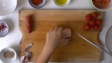 Looking-down-on-hands-of-male-chef,-cutting-chicken-on-wooden-cutting-board