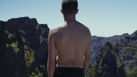 Panning-around-shirtless-man-on-overlook-in-dramatic-mountains,-slow-motion