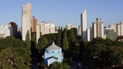 Aerial-descending-drone-shot-inside-of-the-São-Paulo-Cemetery-in-the-Pinheiros-neighborhood-surrounded-by-trees-with-a-blue-building-in-the-middle-on-a-summer-evening-in-Brazil