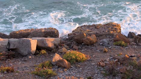 Ocean-waves-gently-hitting-the-rocks-beside-a-dirt-road-at-sunset