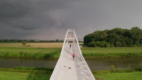 Siguiendo-A-Dos-Ciclistas-Cruzando-Un-Puente-Ciclista-Que-Cruza-El-Tranquilo-Río-Moravia-En-Eslovaquia