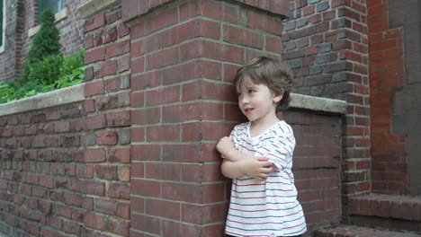 Portrait-of-a-little-boy-with-hands-folded-standing-against-the-red-brick-wall-on-a-bright-sunny-day
