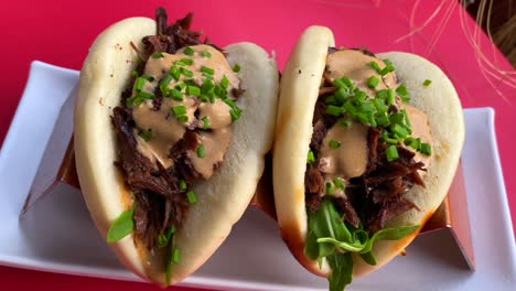 Delicious-bao-buns-with-beef,-rocket-salad,-sauce-and-fresh-chives,-asian-cuisine-in-a-restaurant,-4K-shot