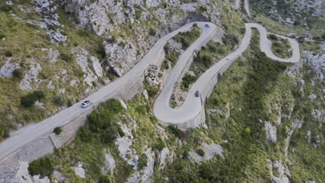 Birds-eye-drone-view-of-a-car-going-down-windy-corners-of-a-mountain-road-in-Sa-Calobra,-Mallorca,-Spain