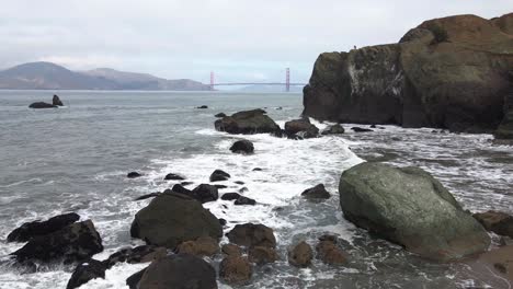 Aerial-drone-view-over-rocks-and-waves-the-Golden-gate-bridge-in-the-background