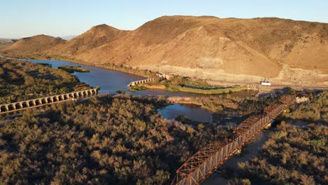 Aerial-view-of-the-Historic-Gillespie-Dam-and-Bridge-along-old-US-hwy-80-with-a-view-of-the-Gila-river,-and-mountains-in-the-background