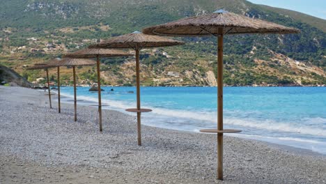 Wooden-beach-umbrellas-on-the-Agia-Kiriaki-Beach-by-the-clear-blue-waves--Wide