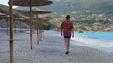 An-Adult-Tourist-Man-Walking-Relaxed-Along-The-Pebbled-Seashore-On-A-Beautiful-Sunny-Day-At-Agia-Kiriaki-Beach,-Zola-In-Kefalonia,-Greece