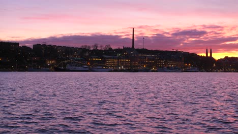 Schwenken-über-Den-Farbenfrohen-Sonnenuntergang-Und-Die-Ostsee-Mit-Den-Lichtern-Der-Stadt-Im-Hintergrund-In-Stockholm,-Schweden