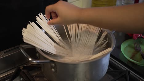 Female-Hand-Placing-Raw-Spaghetti-Noodles-Into-Large-Pot-With-Water-On-Cooker