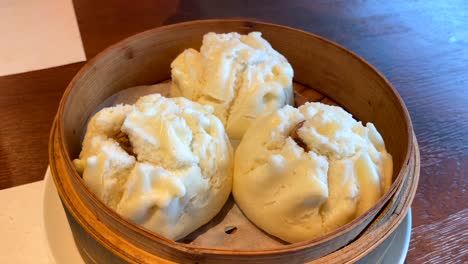 Hot-bao-buns-with-spiced-pork-in-a-bamboo-basket,-man-hand-opening,-steamed-buns-in-a-restaurant,-traditional-asian-cuisine,-4K