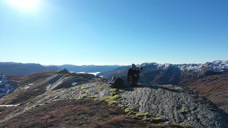 Landscape-photographer-with-telezoom-and-tripod-on-tall-mountain-peak-during-fall-season---Gentle-orbit-around-person-and-in-front-of-lens-with-sunshine-and-stunning-landscape-all-around---Norway