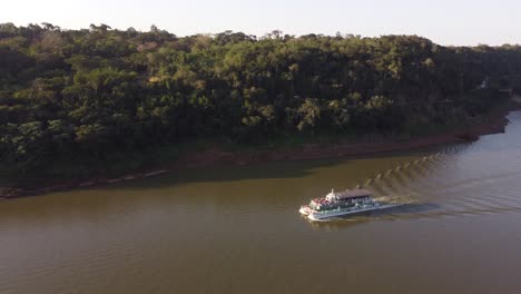 Drone-tracking-shot-of-tourist-boat-cruising-on-brown-colored-dirty-river-at-sunset---Border-between-Argentina-and-Brazil-in-America