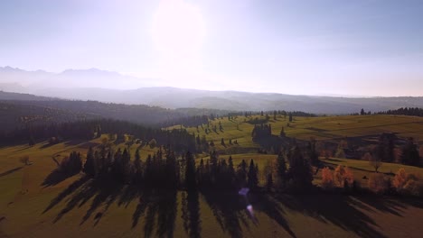Aerial-shot-of-stunning-mountains-landscape,-green-fields,-long-shadows,-forests-and-sunset