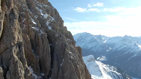 Aufsteigender-Schuss-Des-Felsigen-Fassa-berges-Mit-Schneebedeckter-Bergkette-Im-Hintergrund-Bei-Sonnenlicht