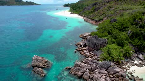 Aerial-View-of-Rocky-Coastline-on-Seychelles-island-with-boat-anchored-and-woman-walking-on-secluded-beach