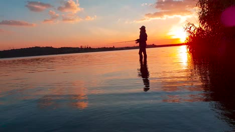 Ein-Mädchen,-Das-In-Einem-Ruhigen-See-Bei-Einem-Perfekten-Sonnenuntergang-über-Dem-Wasser-Fischt