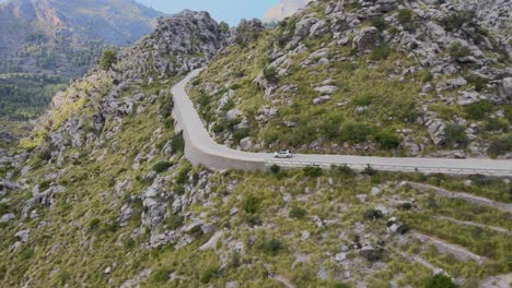 Panorama-drone-shot-of-mountains-with-a-winding-road-following-a-car-going-down-in-Sa-Calobra,-Mallorca,-Spain