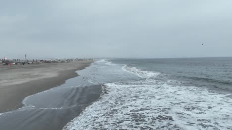 Low-Dolly-Aus-Der-Luft-Nach-Vorne-über-Den-Strand-Von-Pucusuna-Beach-In-Peru-Lima-Mit-Ruhigen-Wellen-Und-Gebäuden-Entlang-Der-Promenade