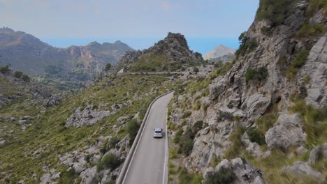 Drone-shot-from-behind-following-a-car-on-a-windy-mountain-road-in-Sa-Calobra,-Mallorca,-Spain