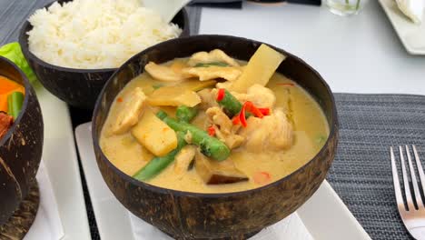 Würzige-Thailändische-Kokosnusssuppe-Mit-Hühnchen,-Bambus-Und-Gemüse-In-Einer-Schönen-Kokosnussschale,-Warmes-Gericht-Im-Thailändischen-Küchenrestaurant,-4k-aufnahme