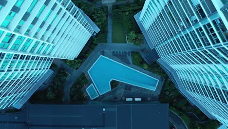 Top-down-flying-upwards-shot-of-swimming-pool-in-between-two-apartment-buildings,-symmetrical-look