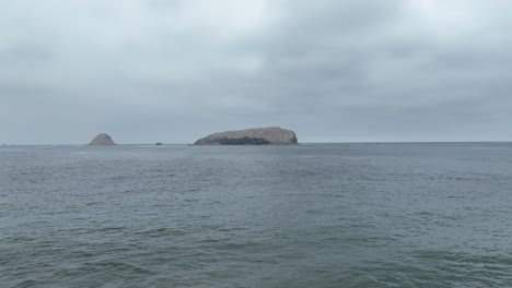 Low-Dolly-Aus-Der-Luft-Nach-Vorne-Geschossen-Vom-Strand-In-Pucusuna-Strand-In-Peru-Lima-über-Dem-Meer-Mit-Blick-Auf-Eine-Insel-Mit-Felsen-Und-Booten-Im-Hintergrund