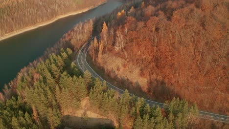 An-aerial-ascending-drone-view-of-cars-driving-on-a-winding-road-alongside-a-lake-in-late-autumn