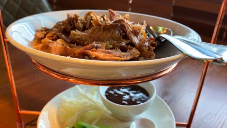 Traditional-crispy-peking-duck-with-steamed-pancakes,-onion,-cucumber-and-hoisin-sauce,-delicious-Asian-dish-served-on-a-three-floor-tray-tower,-4K-shot