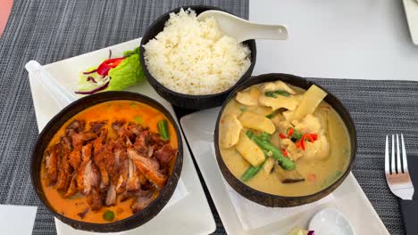 Pato-Crujiente-En-Salsa-De-Curry-Rojo-Con-Arroz-Y-Sopa-De-Coco-Tailandesa-Picante-Con-Pollo-Y-Verduras-En-Un-Tazón-De-Coco,-Restaurante-De-Cocina-Tailandesa,-Toma-De-4k