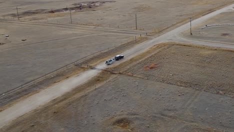 A-small-boat-attached-to-the-back-of-a-van-driving-down-a-dirt-road-in-the-country-near-Alberta-Canada-filmed-in-the-air-from-a-drone