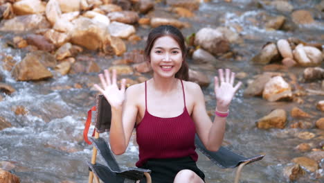 Asian-woman-in-red-sitting-on-a-chair-with-big-rocks-and-water-slow-splashing-for-relaxing-and-happiness-in-the-vacation-summertime