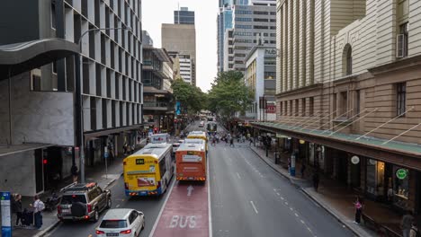 Timelapse-shot-of-busy-road-traffics,-looking-straight-at-Adelaide-street-with-buses-and-cars-driving-across-and-people-rushing-at-central-business-district,-rapid-population-growth-of-Brisbane-city